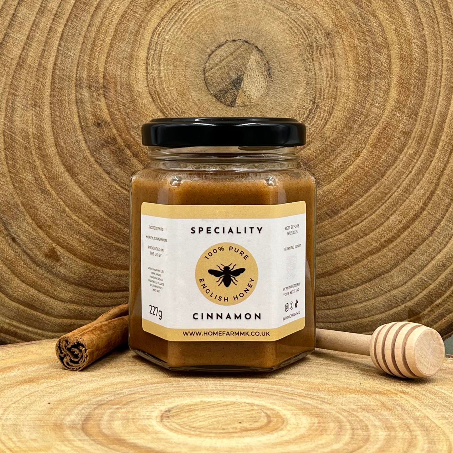 Jar of cinnamon honey on a wooden surface with a honey dipper and stick of cinnamon