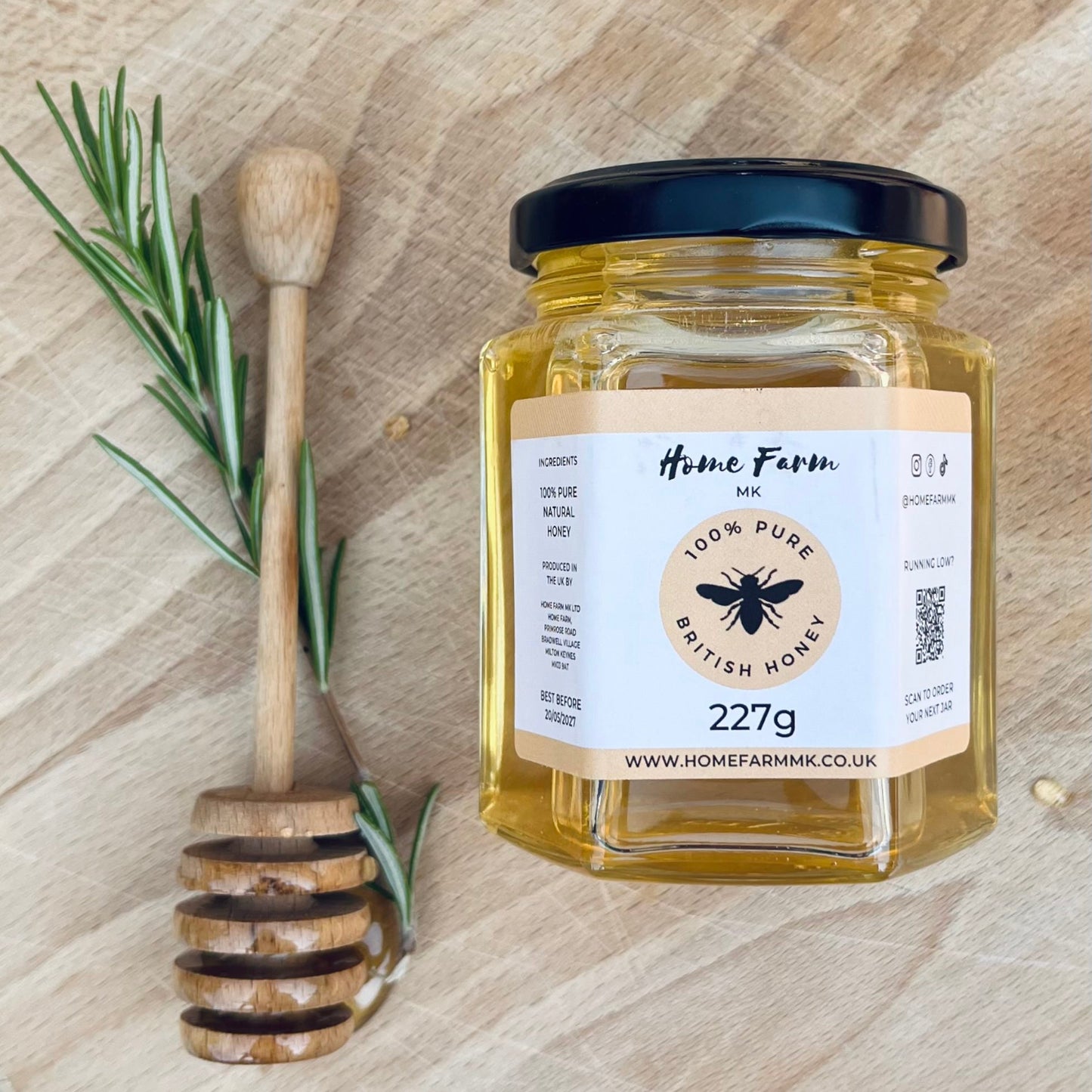 Jar of honey with a honey dipper and rosemary on a wooden surface