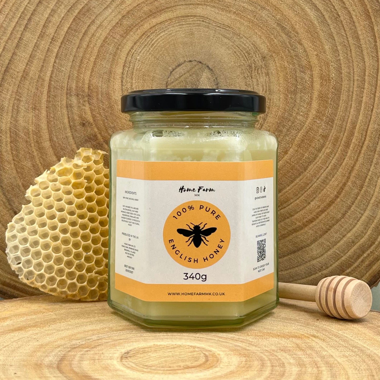A jar of naturally set honey with a honey dipper and piece of honeycomb on a wooden surface