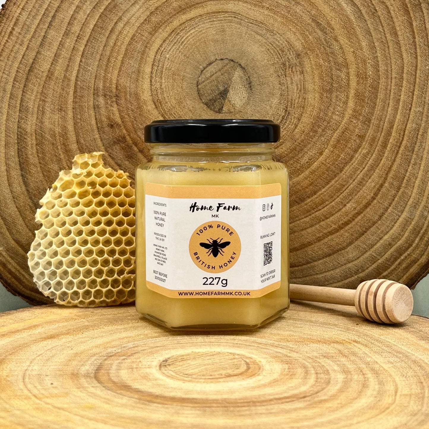 Jar of soft set honey with honeycomb and a honey dipper on a wooden surface