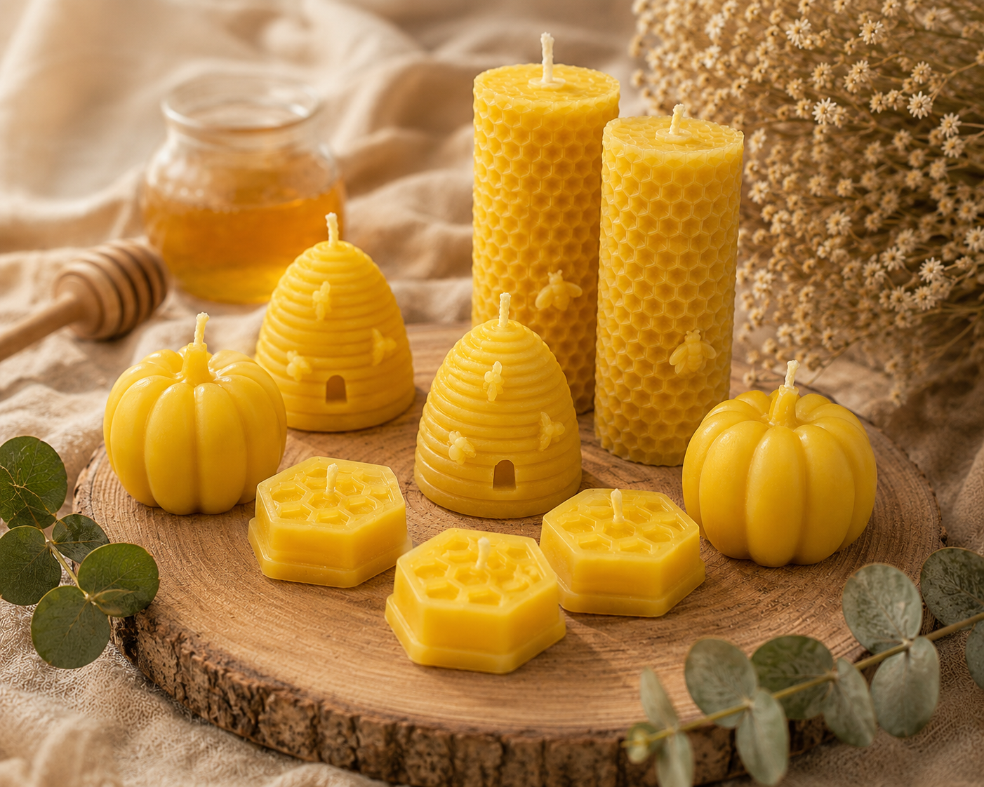 A styled arrangement of yellow honey-themed beeswax candles on a round wood slice, including beehive-shaped pillar candles, pumpkin-shaped candles, and hexagonal candles, with honey, dried flowers, and greenery in the background.