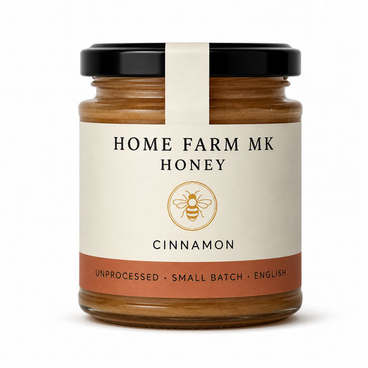 A glass jar of Home Farm Mk Cinnamon Honey with a black lid and a cream-colored label featuring a gold bee logo.