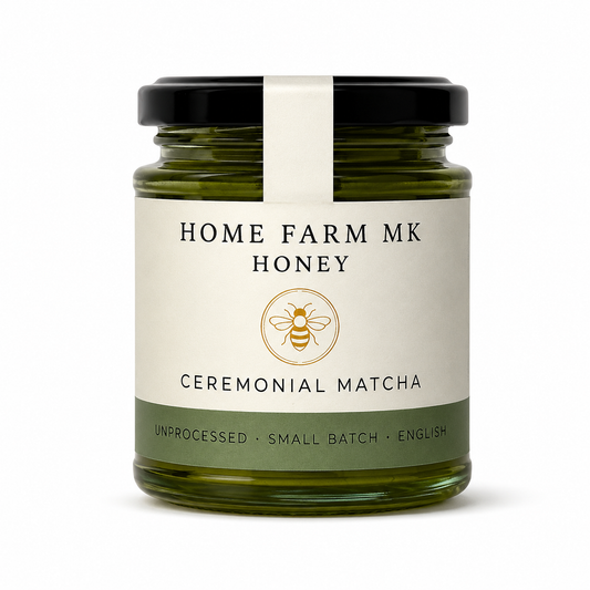 A glass jar of Home Farm MK Honey with Ceremonial Matcha flavor, featuring a cream-colored label with a gold bee logo and a black lid, set against a plain white background.