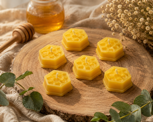 Five yellow honeycomb-shaped beeswax candles arranged on a round wooden slice, with a honey dipper, honey jar, dried flowers, and green leaves in a rustic styled setting.