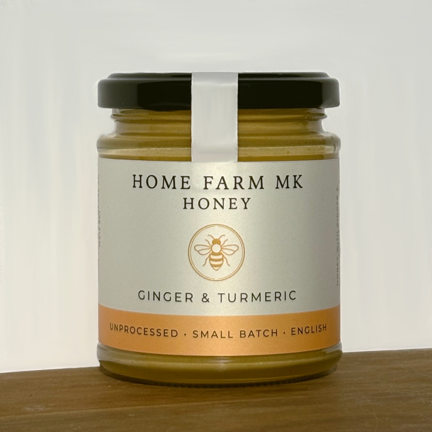 Jar of Home Farm MK Honey with ginger and turmeric flavour on a wooden surface.