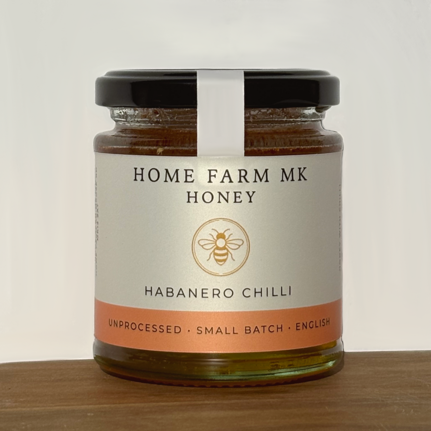 Jar of Home Farm MK Honey with habanero chilli flavour on a wooden surface.