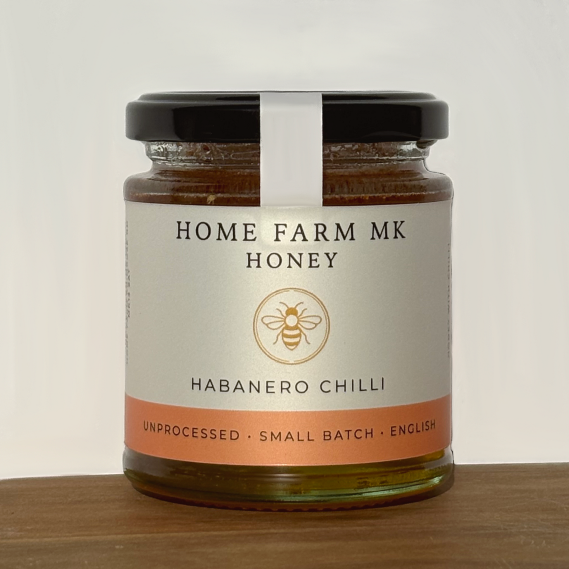 Jar of Home Farm MK Honey with habanero chilli flavour on a wooden surface.
