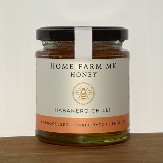 Jar of Home Farm MK Honey with habanero chilli flavour on a wooden surface.