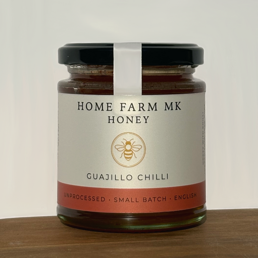 Jar of Home Farm MK Hot Honey infused with Mild Guajillo Chilli on a wooden surface