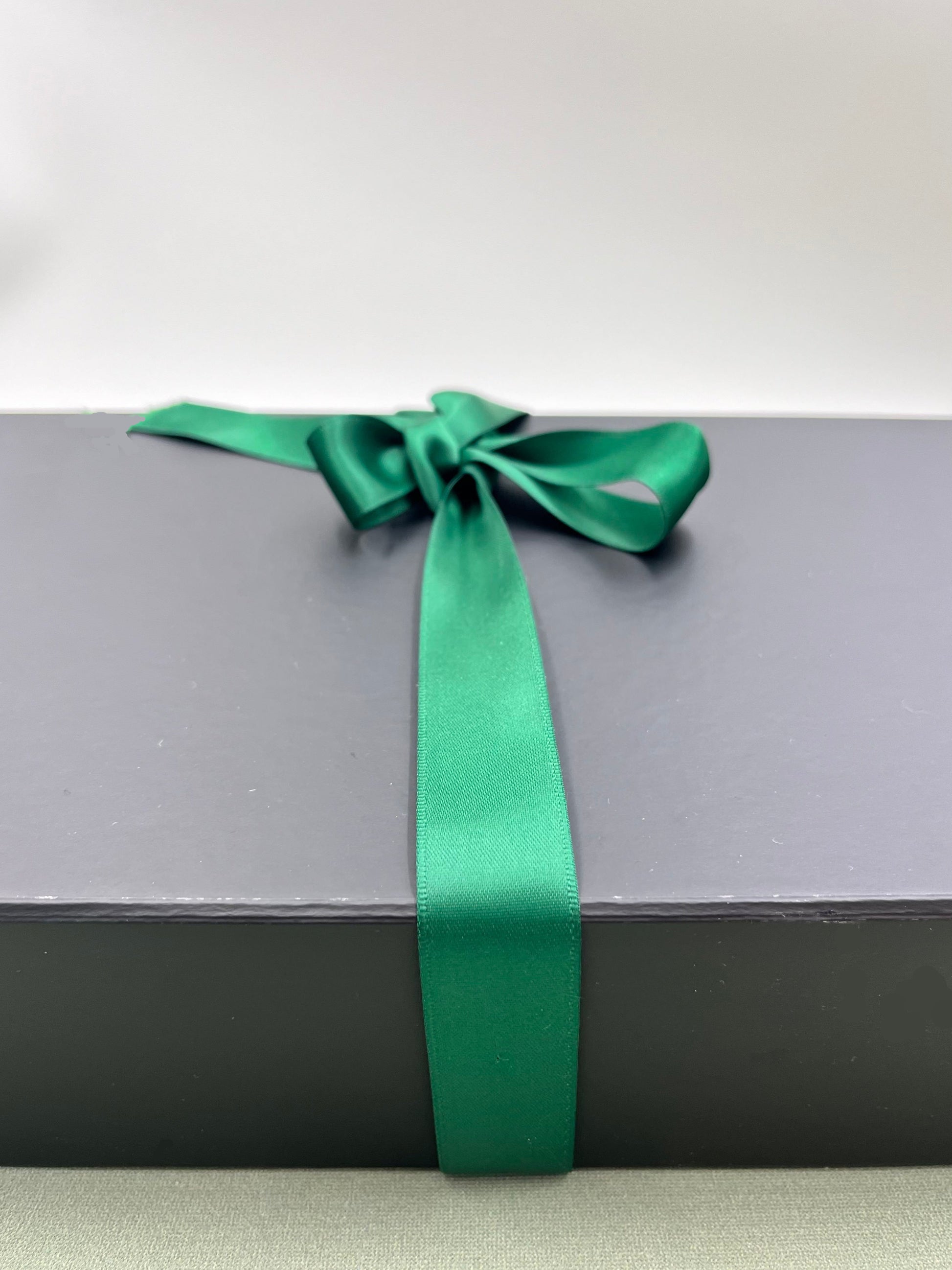Black gift box with a green satin ribbon on a light grey background