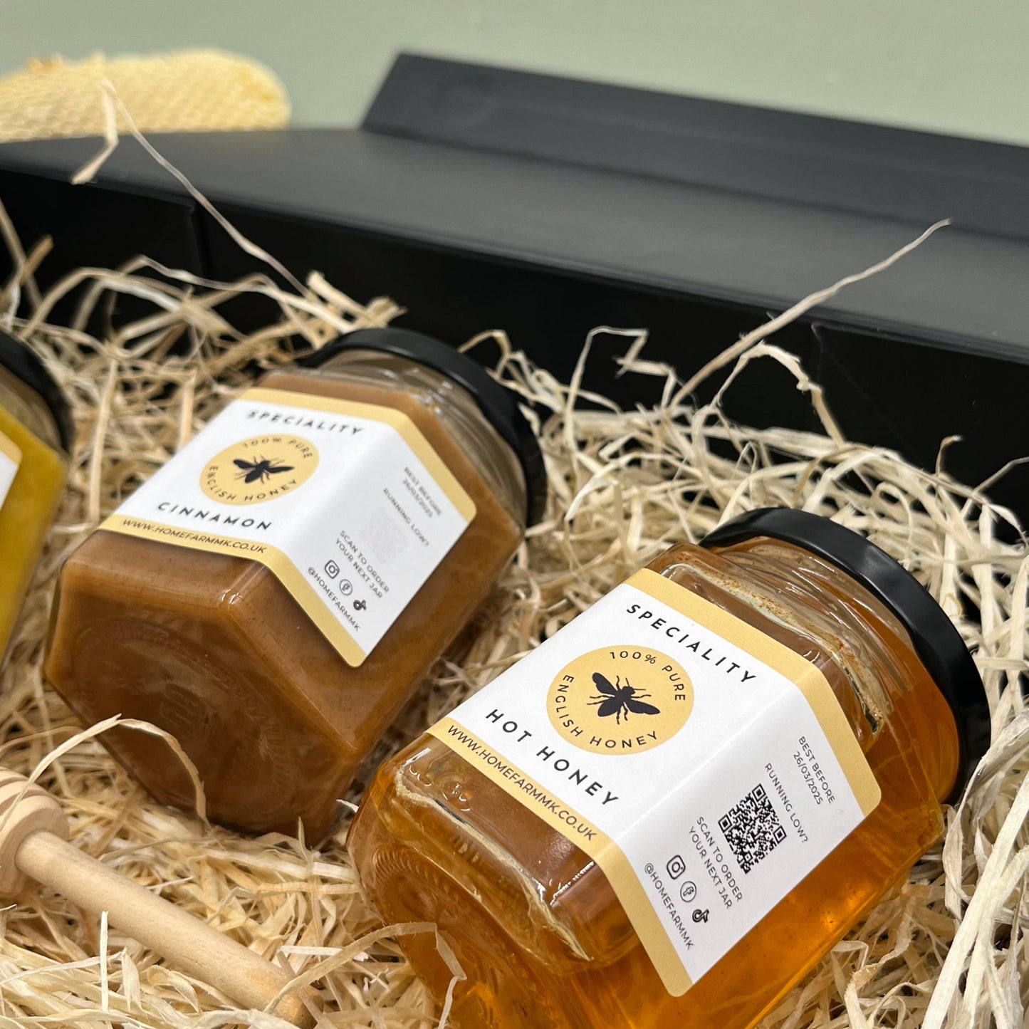 A jar of brown cinnamon honey and a jar of orange hot habanero honey presented in a black gift-box