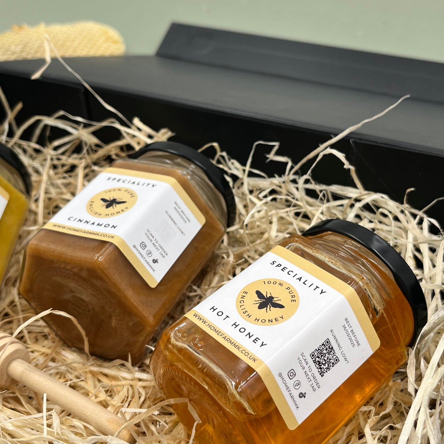 A jar of brown cinnamon honey and a jar of orange hot habanero honey presented in a black gift-box