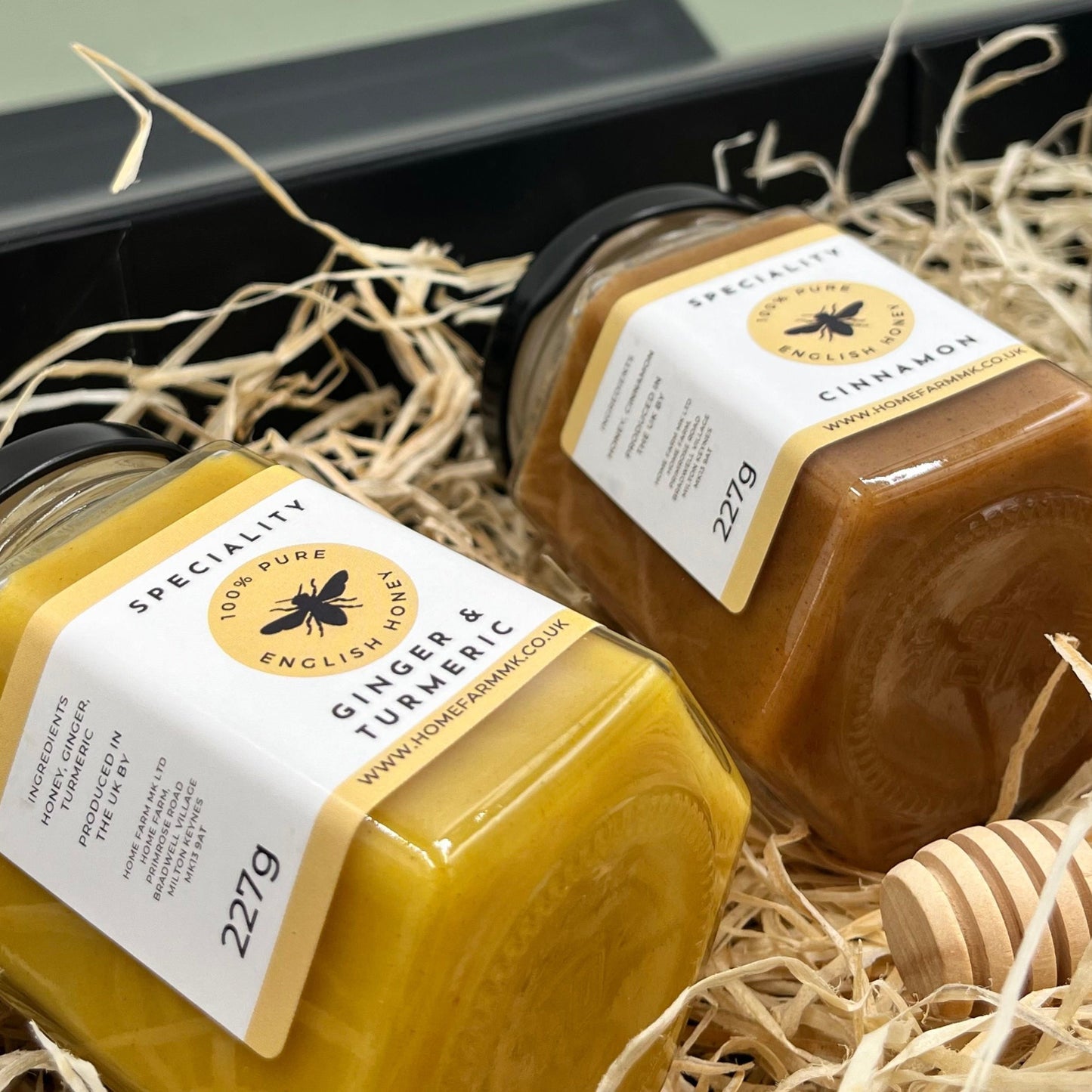 A jar of ginger & turmeric honey and a jar of cinnamon honey on a bed of wood straw inside a black gift box
