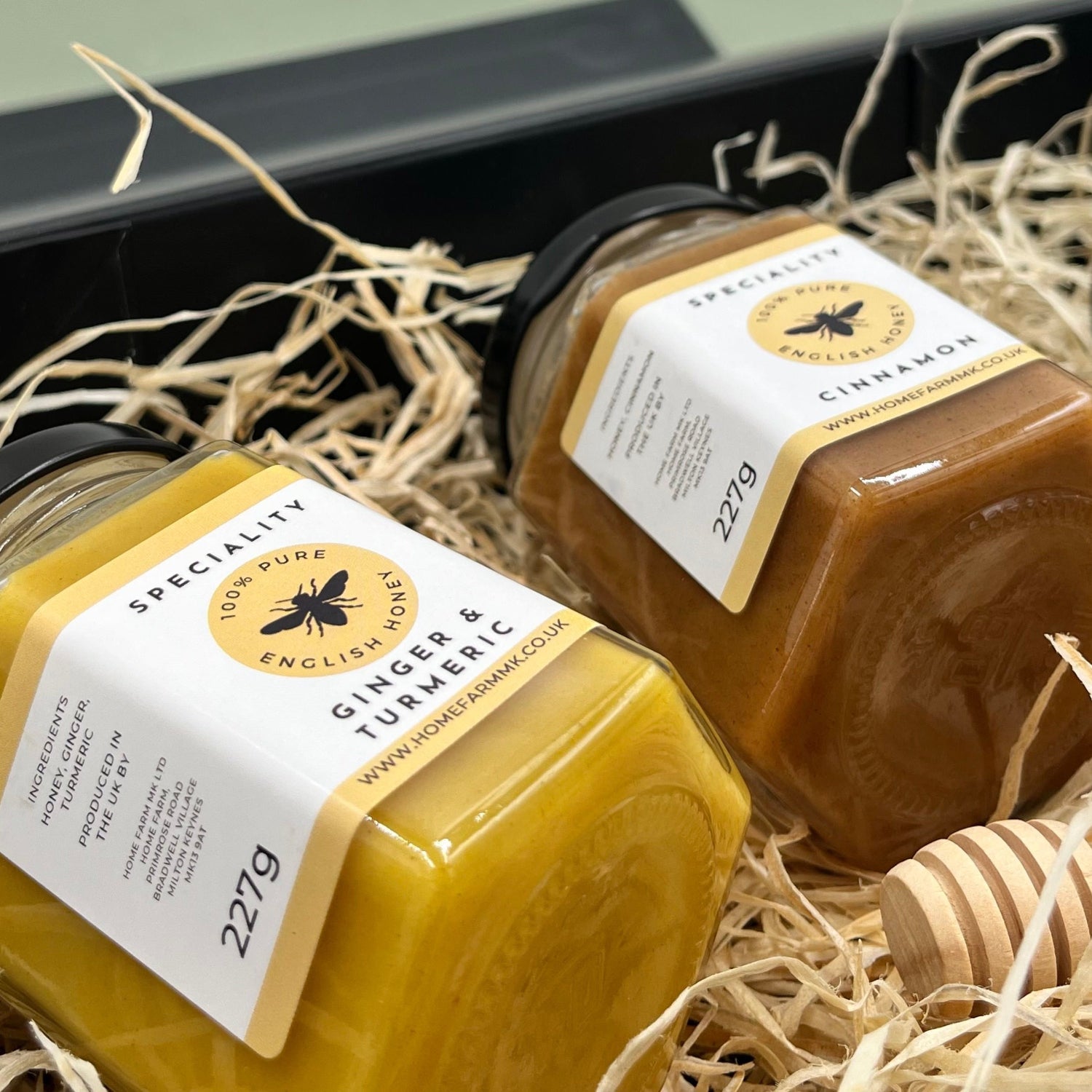 A jar of ginger & turmeric honey and a jar of cinnamon honey on a bed of wood straw inside a black gift box