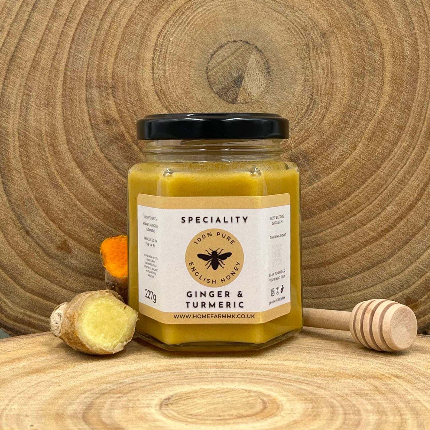 Jar of ginger and turmeric honey on a wooden surface with a honey dipper and fresh slices of ginger and turmeric.