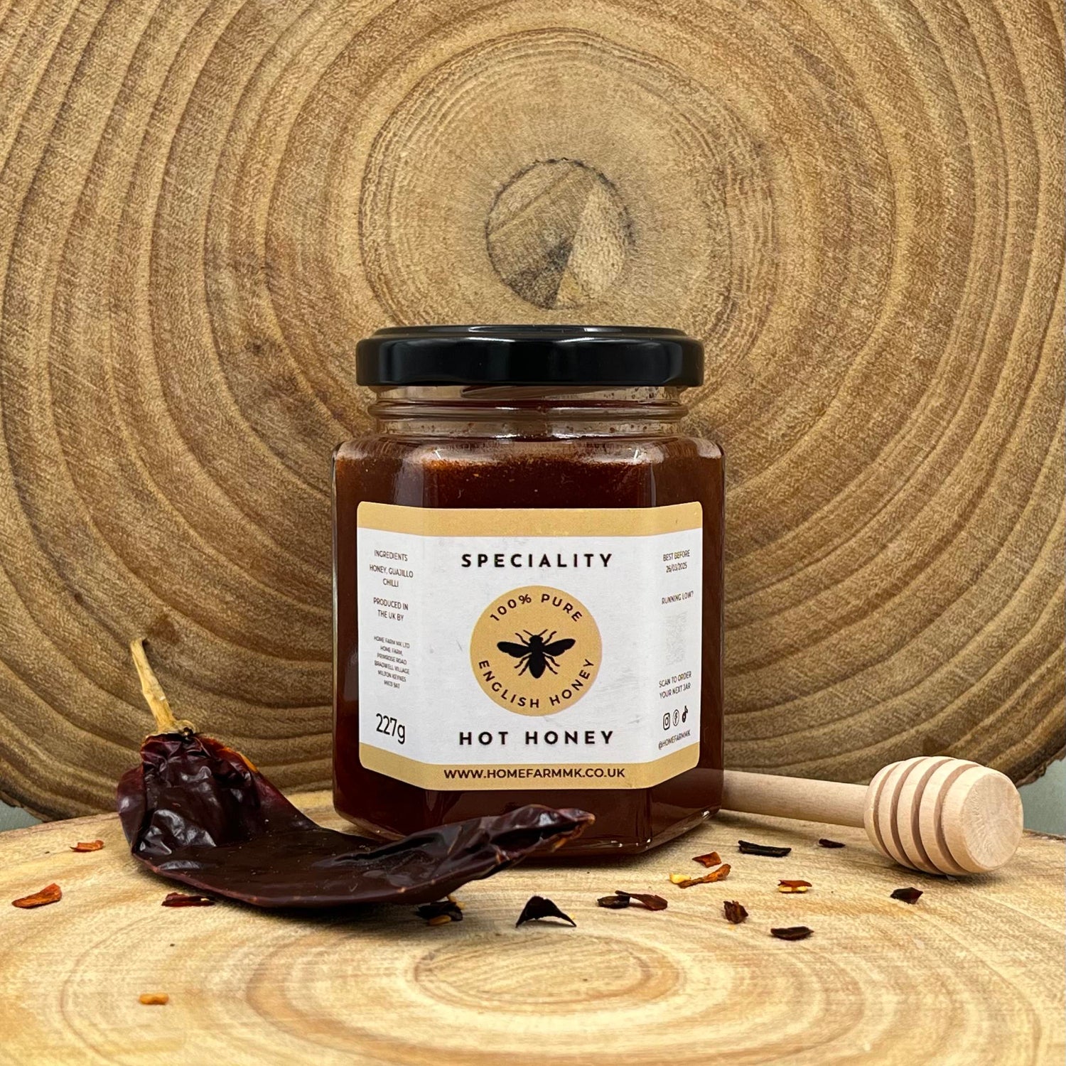 Jar of hot honey infused with smoky Guajillo chilli on a wooden surface with a honey dipper and dried chilli