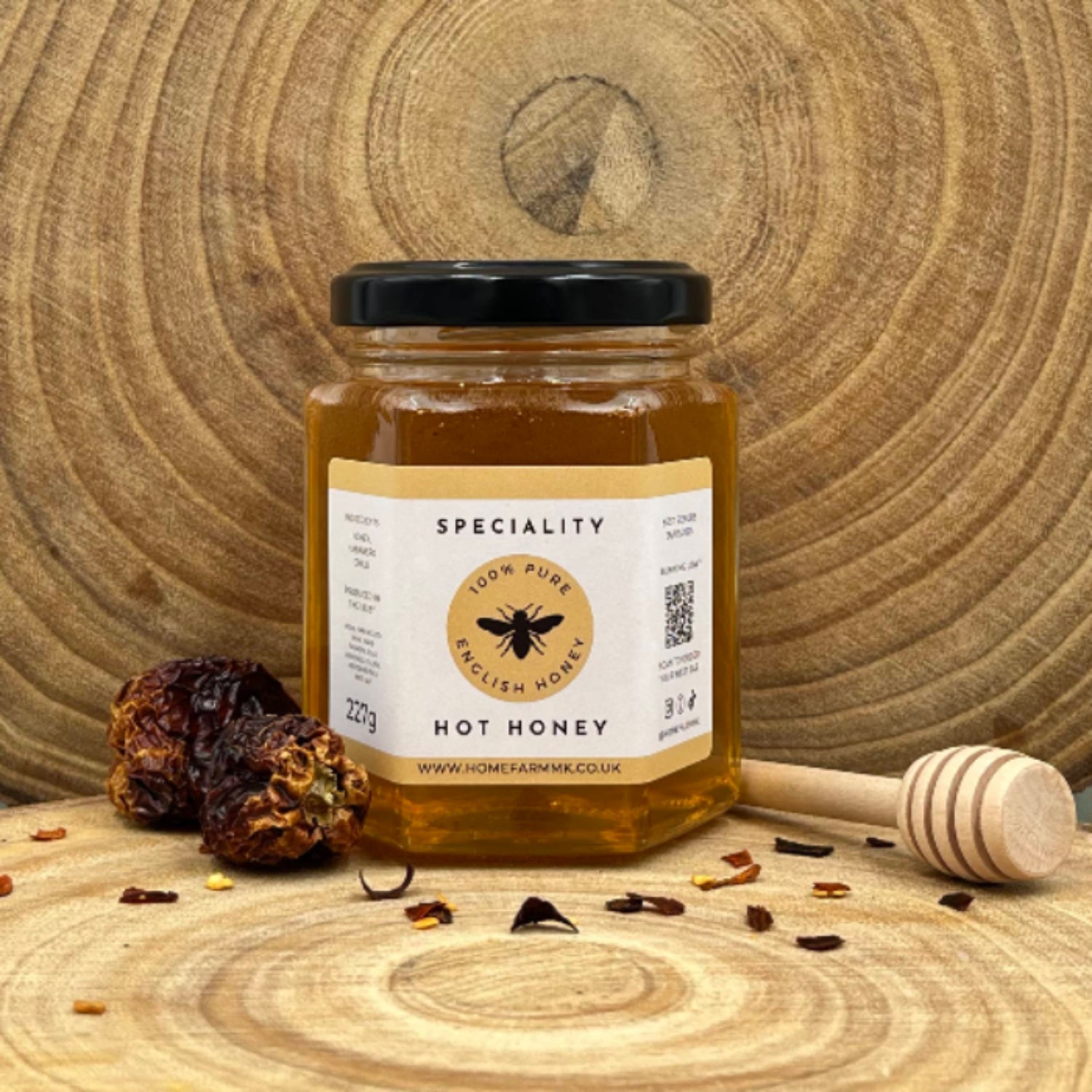 Jar of chilli infused, habanero hot honey on a wooden log slice with a honey dipper and chilli flakes