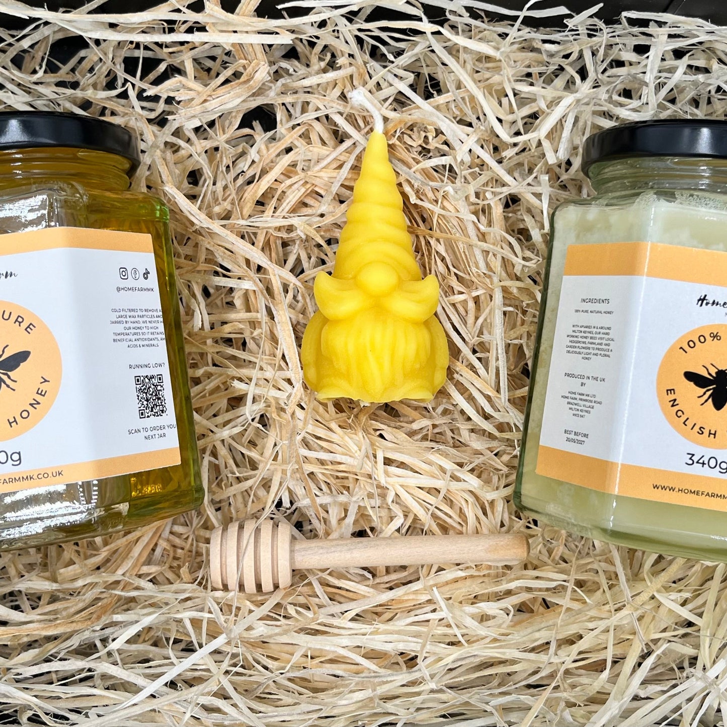 Two jars of honey and a festive gonk shaped beeswax candle on a bed of shredded wood paper inside a gift box.