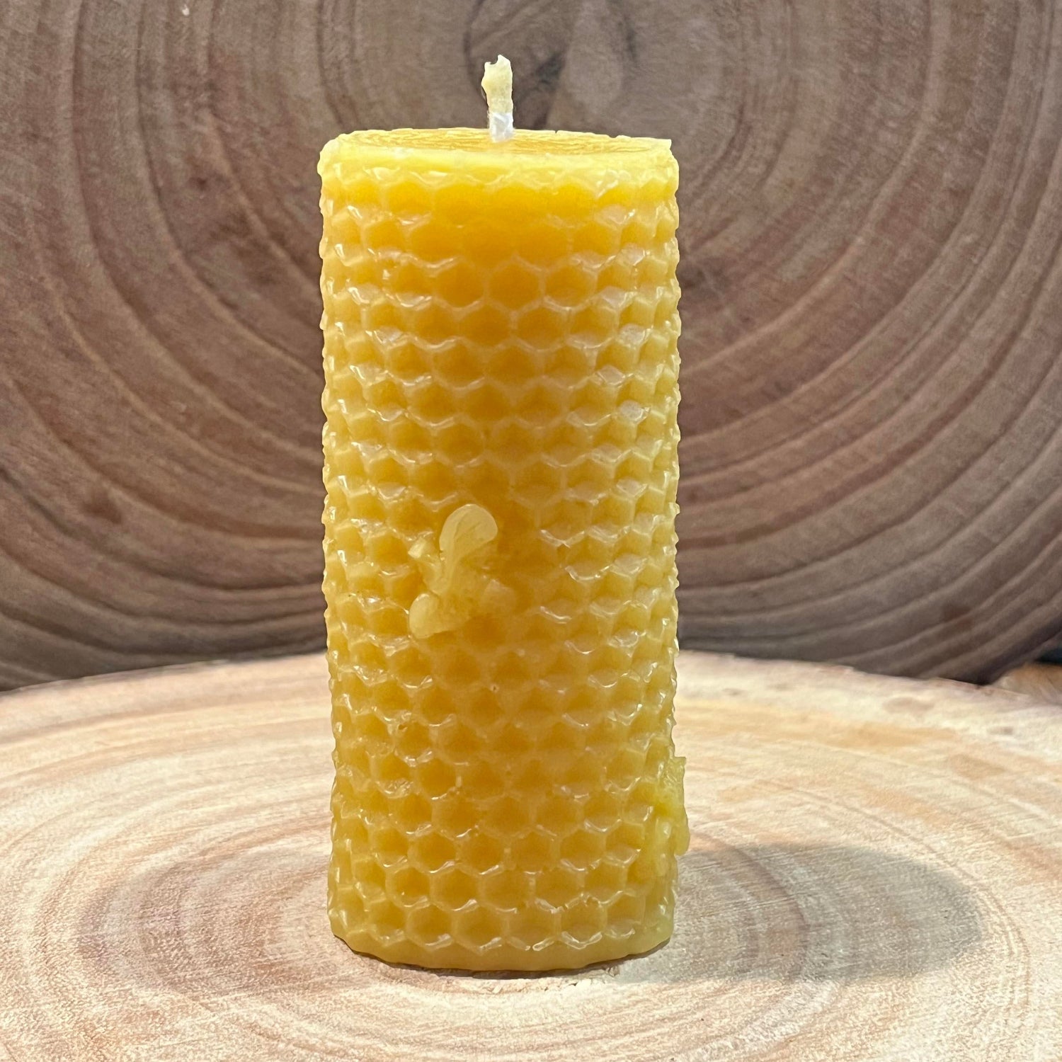 The back of a yellow beeswax pillar candle with a honeycomb effect and small bee details
