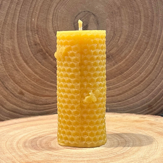 The front of a yellow beeswax pillar candle, with a rolled honeycomb pattern and small bee details