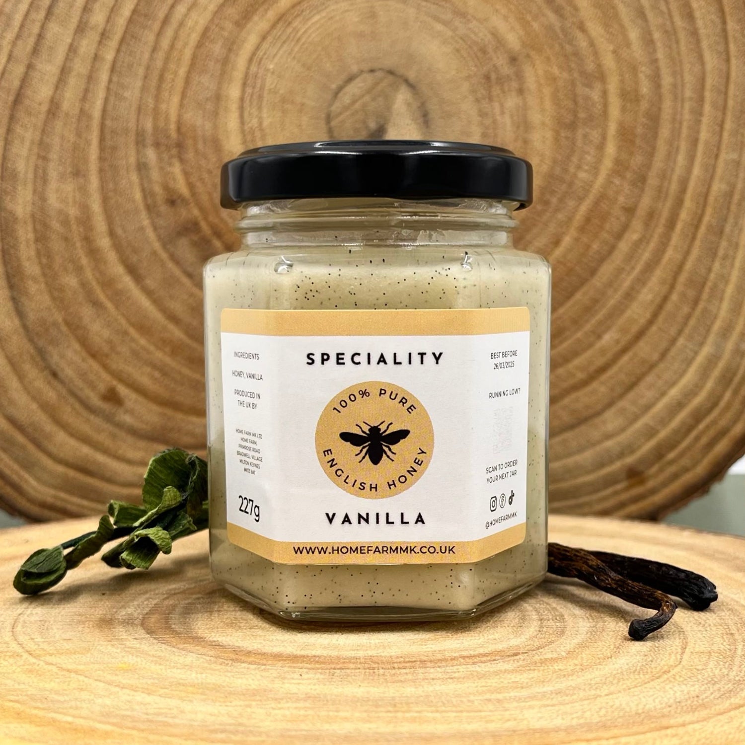 Jar of honey infused with madagascan vanilla beans on a wooden log slice with two vanilla pods 