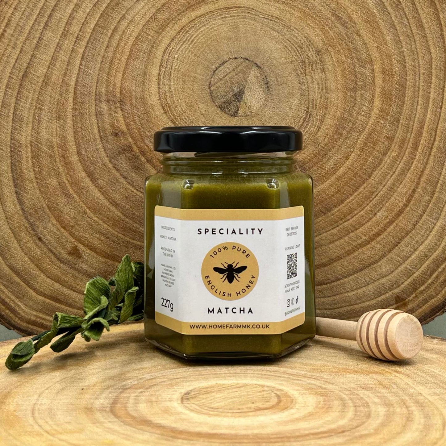 Jar of matcha honey on a wooden surface with a honey dipper and green leaves.