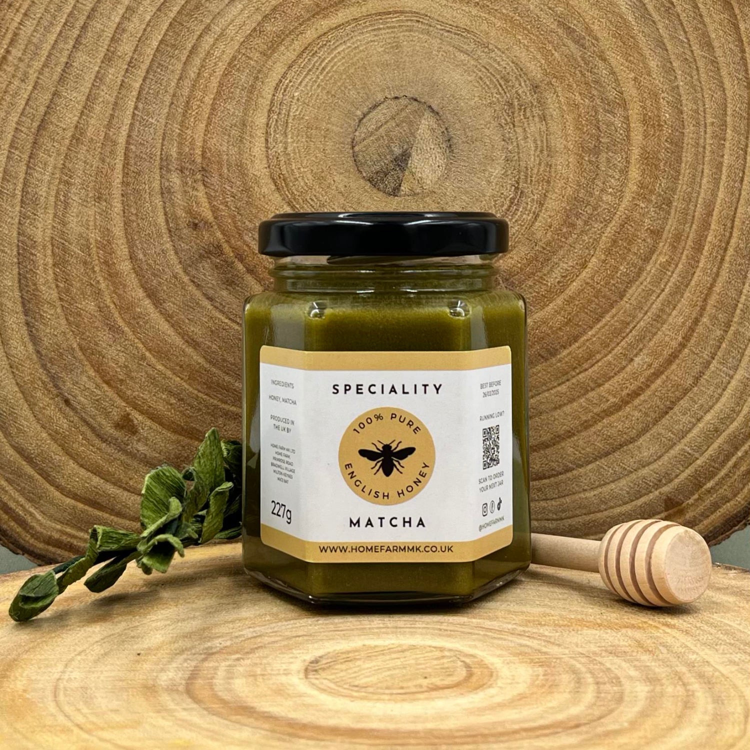 Jar of matcha honey on a wooden surface with a honey dipper and green leaves.