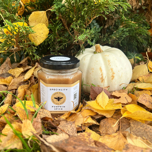 Jar of seasonal pumpkin spice honey on a bed of autumn leaves and a small white pumpkin.