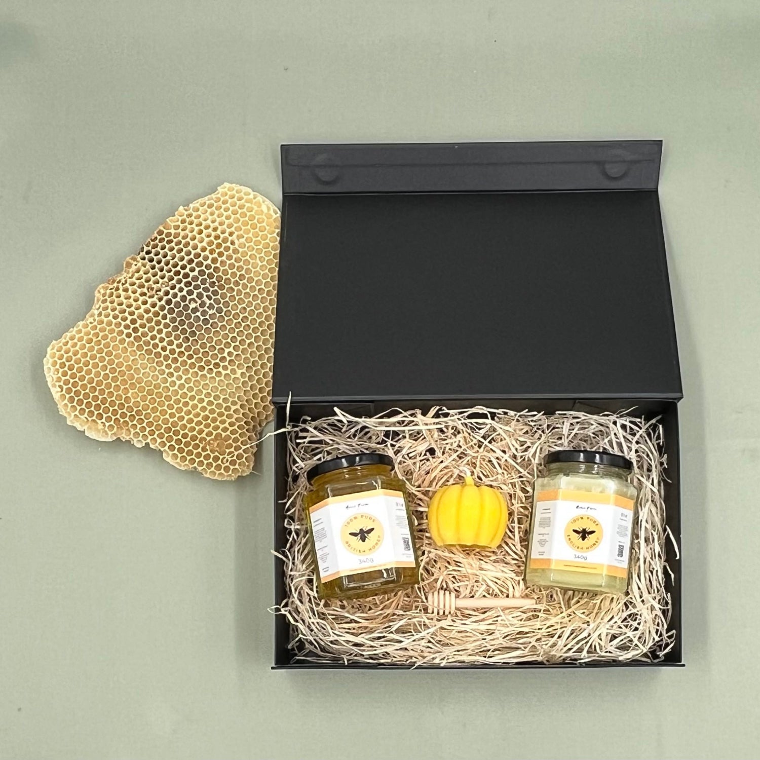 Two jars of honey and a yellow honeycomb pillar candle in a black gift box