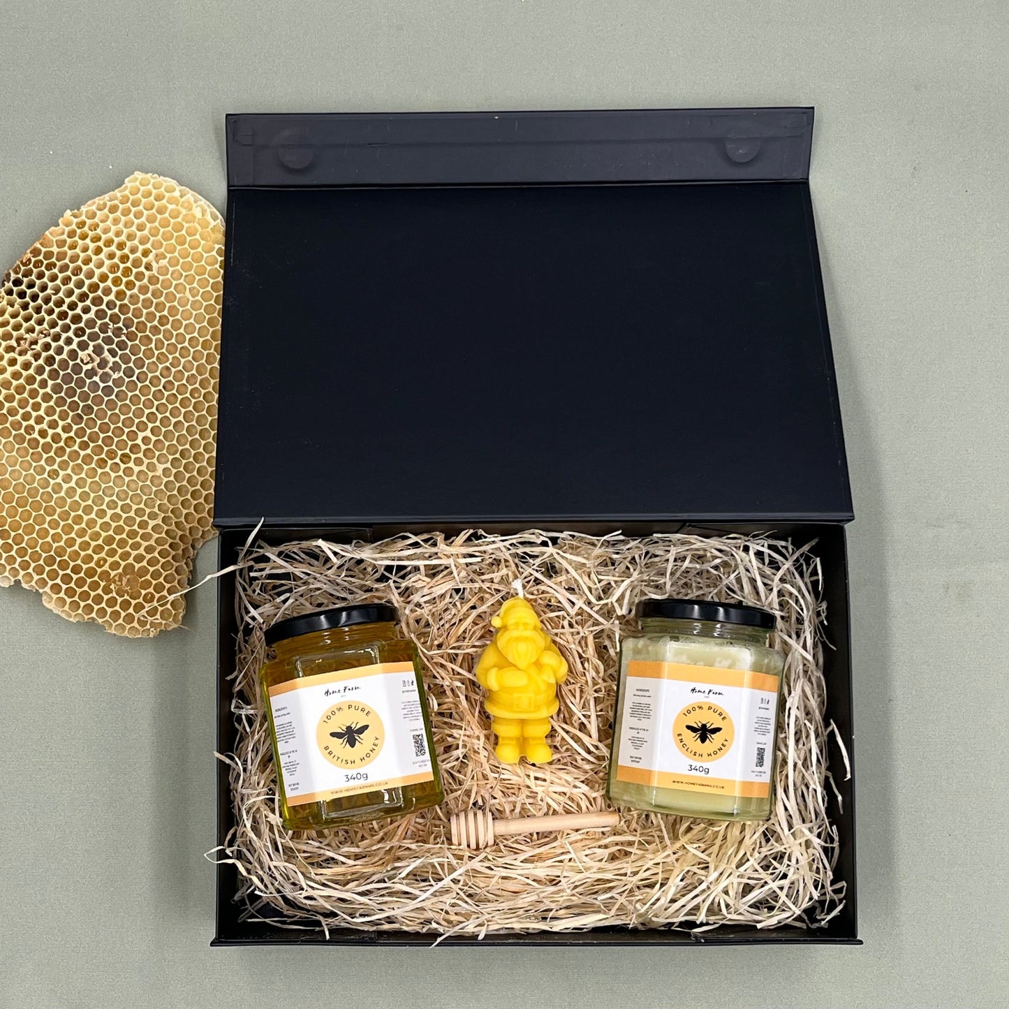 A black gift box with two honey jars, a festive santa-shaped beeswax candle and a wooden honey dipper
