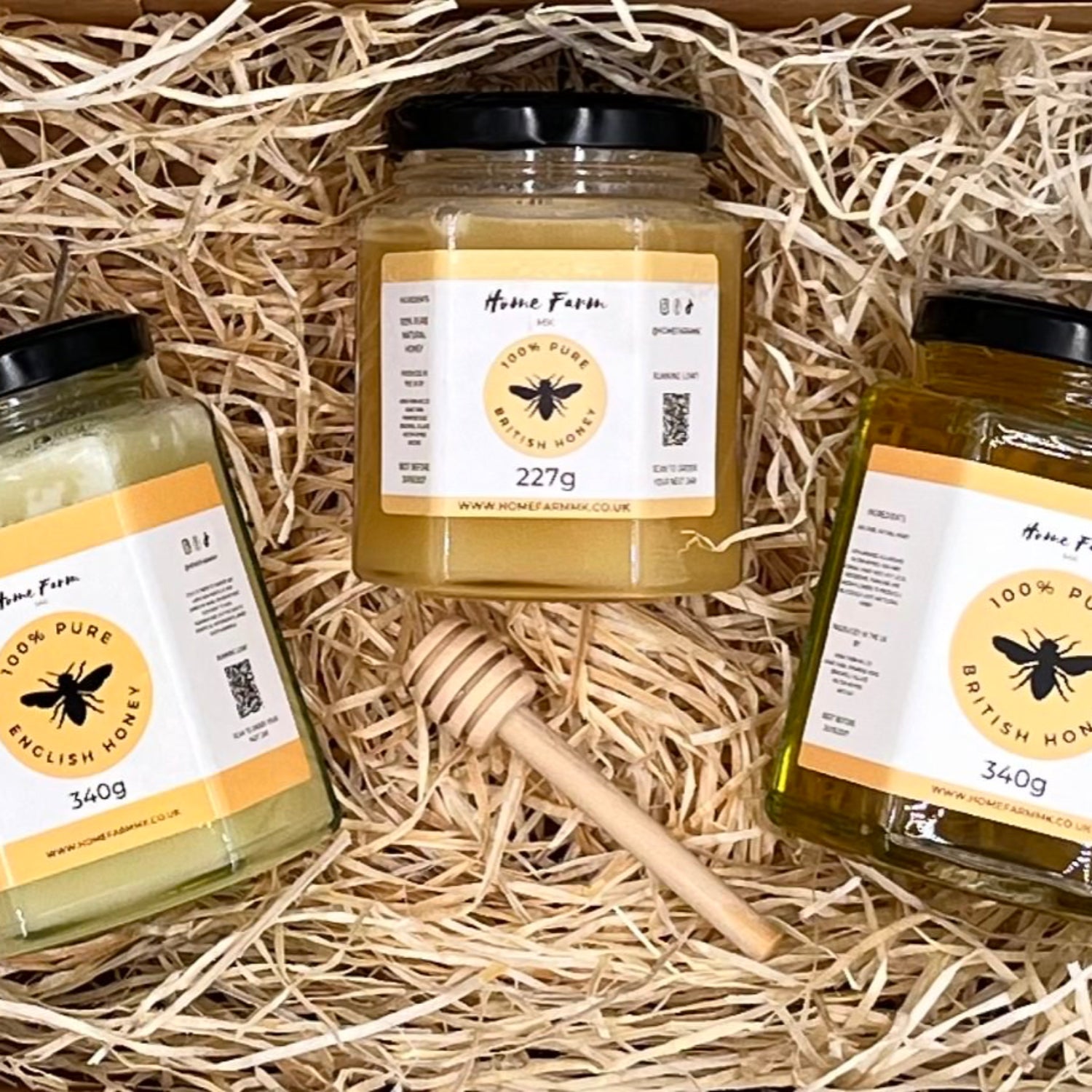 Three jars of honey and a wooden honey dipper on a bed of paper straw laid inside a giftbox - one runny, one set and one soft set jar