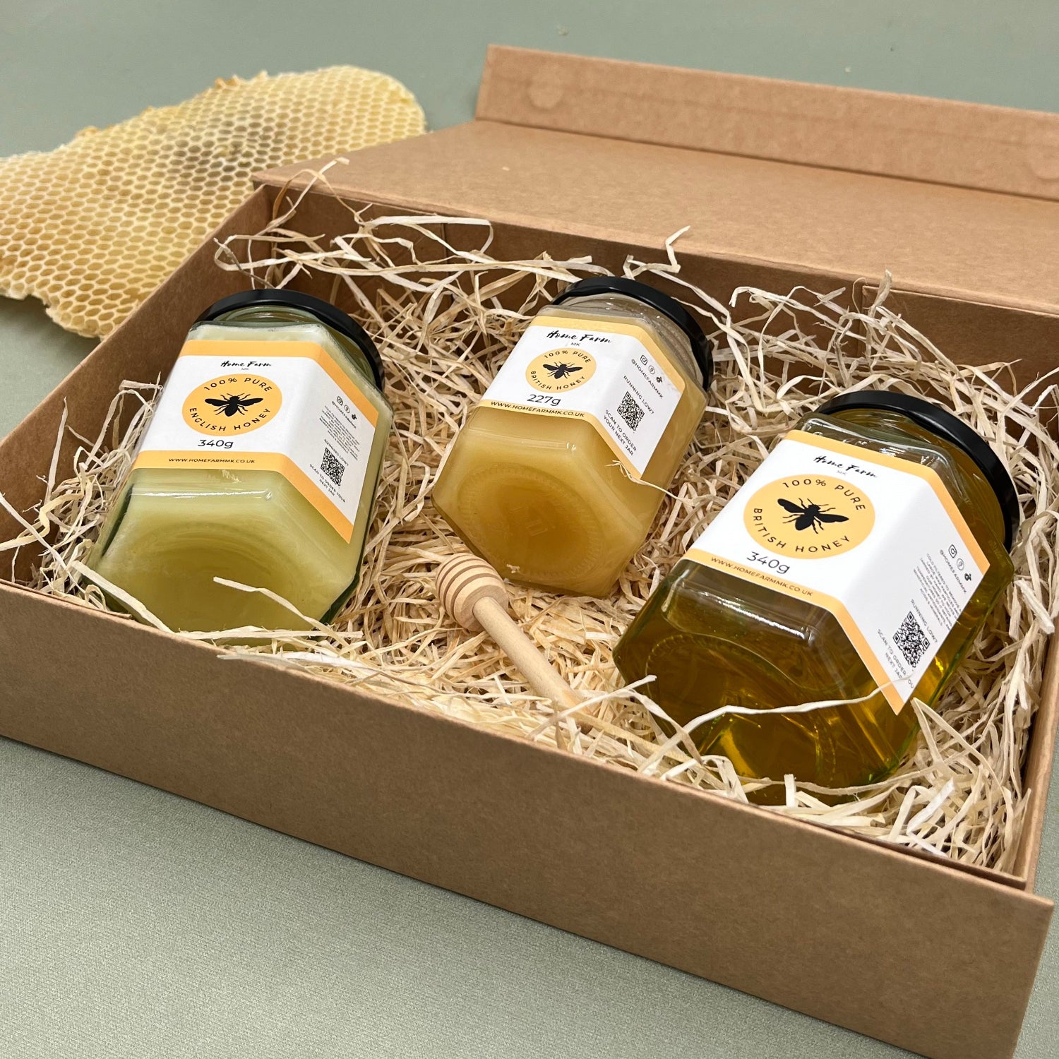 Three jars of honey and a wooden dipper in a gift box with a piece of honeycomb