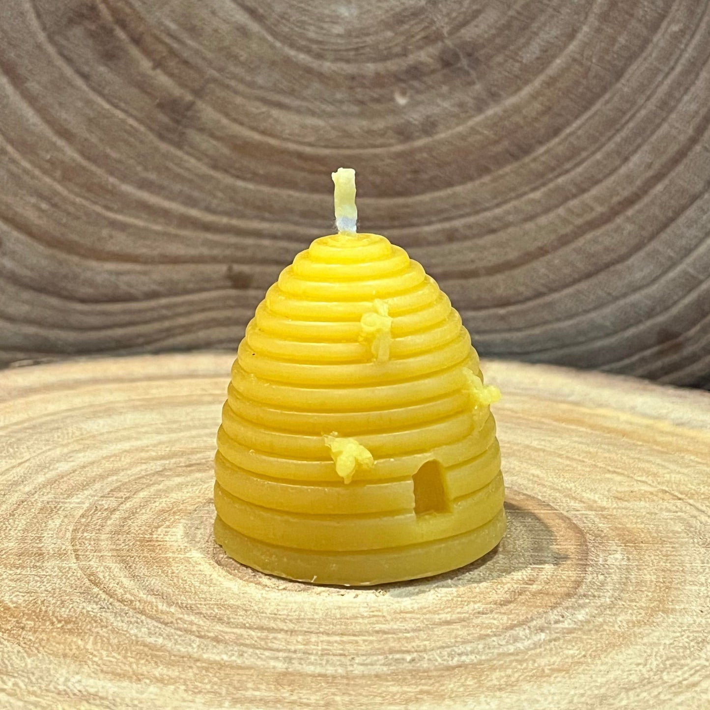 The left hand side of a yellow skep beehive-shaped beeswax candle with small bee details