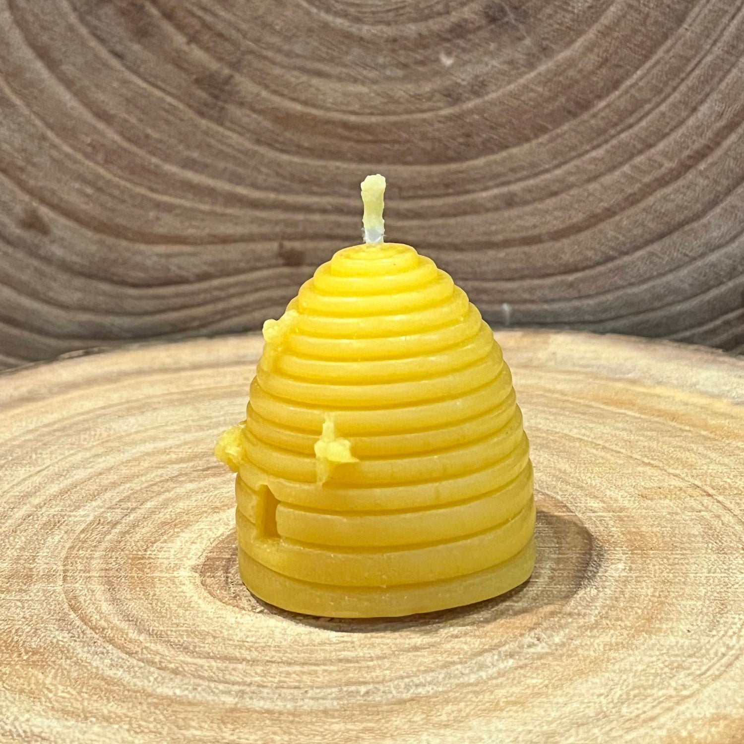 The right hand side of a yellow skep beehive-shaped beeswax candle with small bee details
